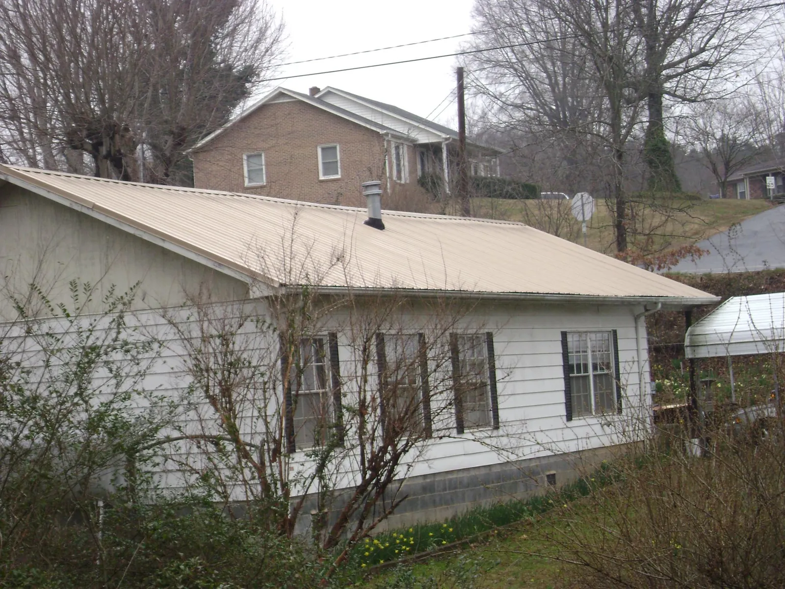 Tan metal roof on a white sided house set into a hillside — Commercial Roofing by Roofing Brothers in Morris