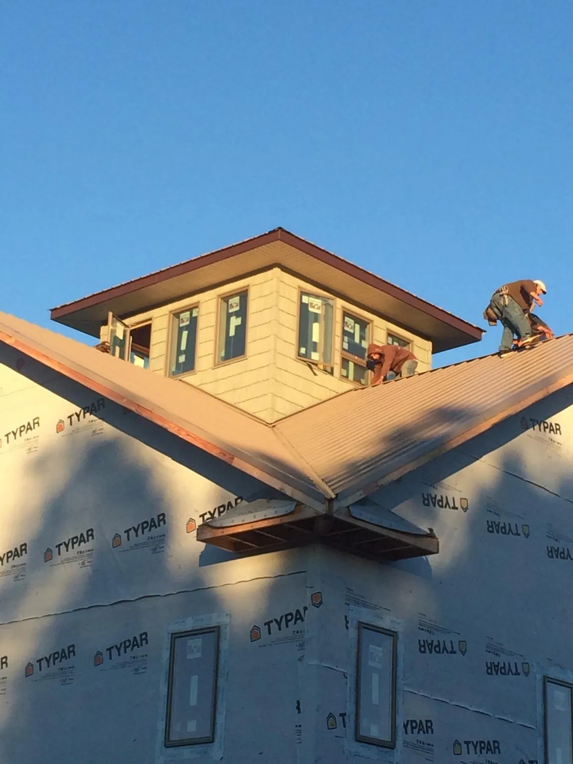 Roofers working around a rooftop cupola on a new metal roof at sunset — Roof Waterproofing in Morris by Roofing Brothers